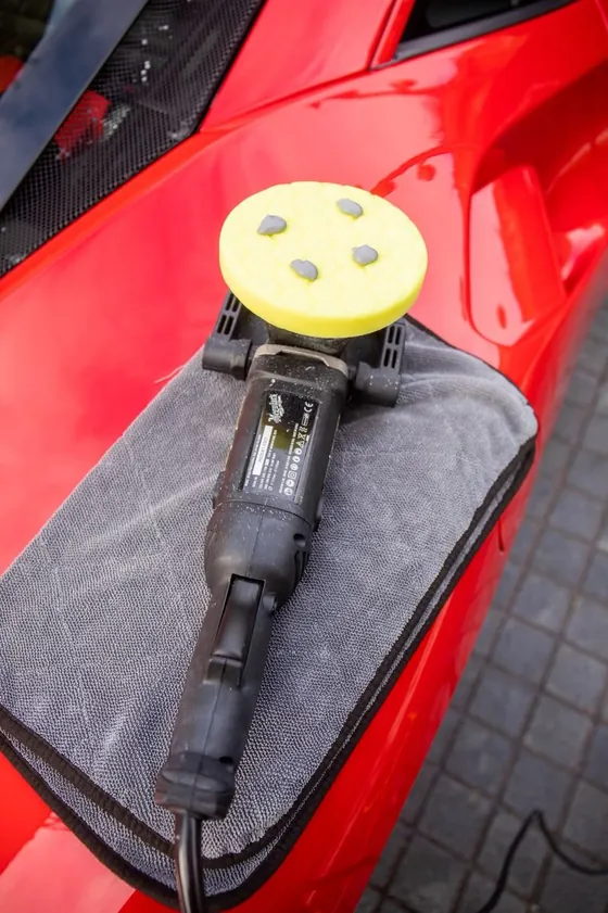 Machine polisher resting on a microfibre towel on a red car before paint correction