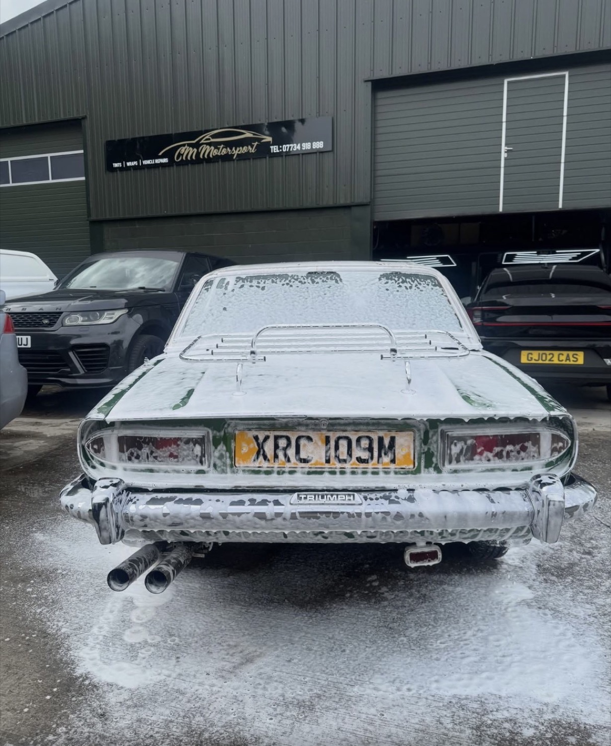 Rear of a classic Triumph Stag during a snow-foam decontamination wash