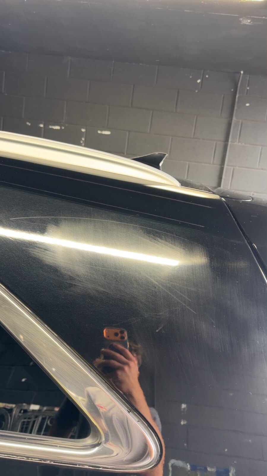 Deep scratches and swirl marks in the black paint on a car's rear quarter panel before any work